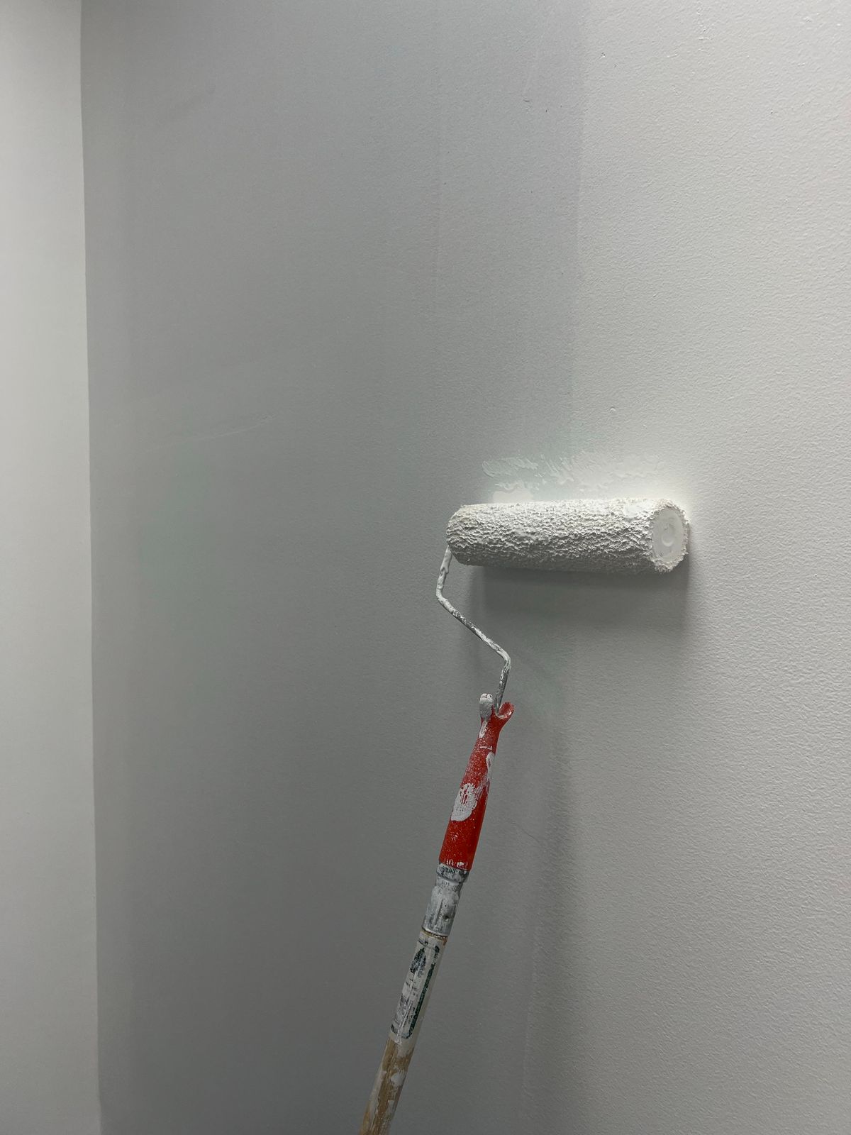 A roller applying white paint to a bedroom wall